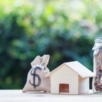 US dollar in a money bag, small residential, house model on table against green nature background.